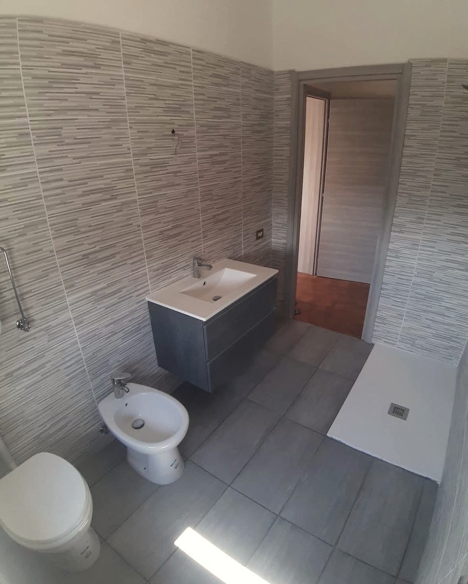 Bagno rifatto con mobile sospeso grigio, sanitari bianchi e piatto doccia